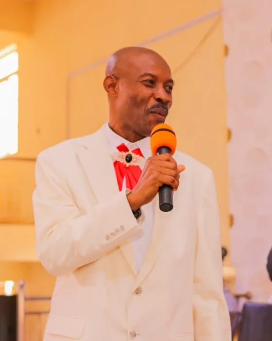 Pastor Emmanuel Mezu speaking at a service, holding a microphone
