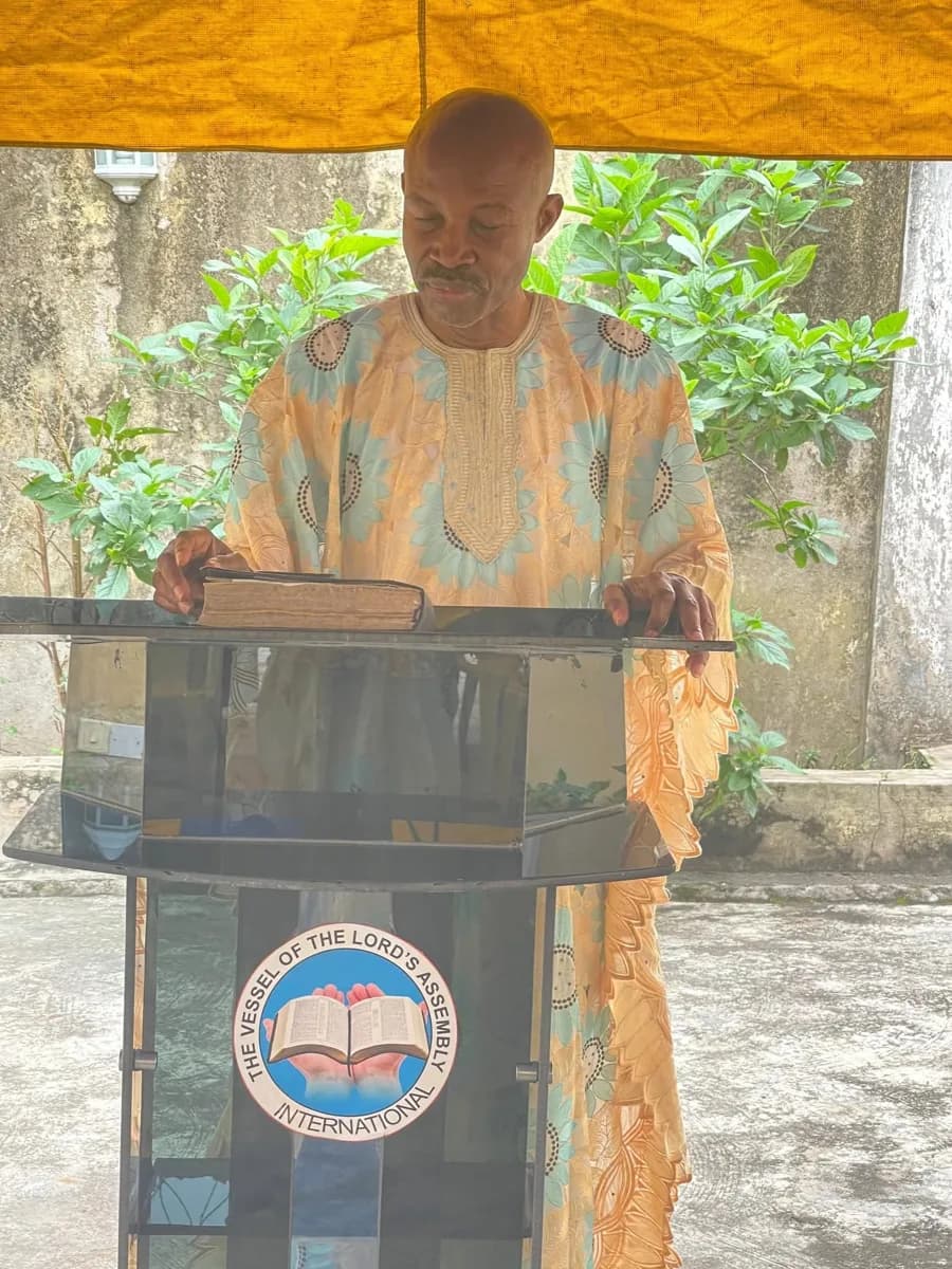 Preaching from the fellowship's pulpit, which carries the church emblem